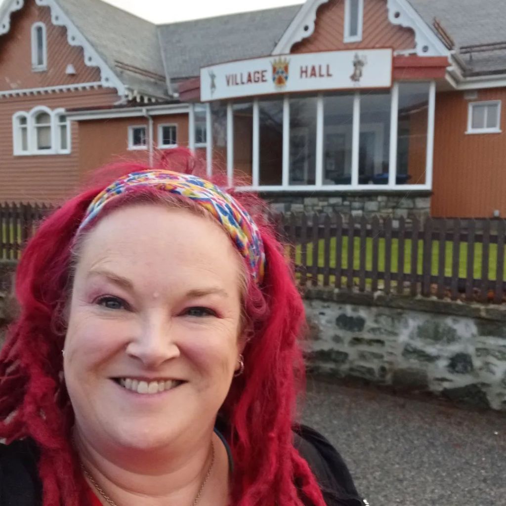 A photo off Pauline Cordiner, storyteller, smiling outside Braemar Village Hall. 