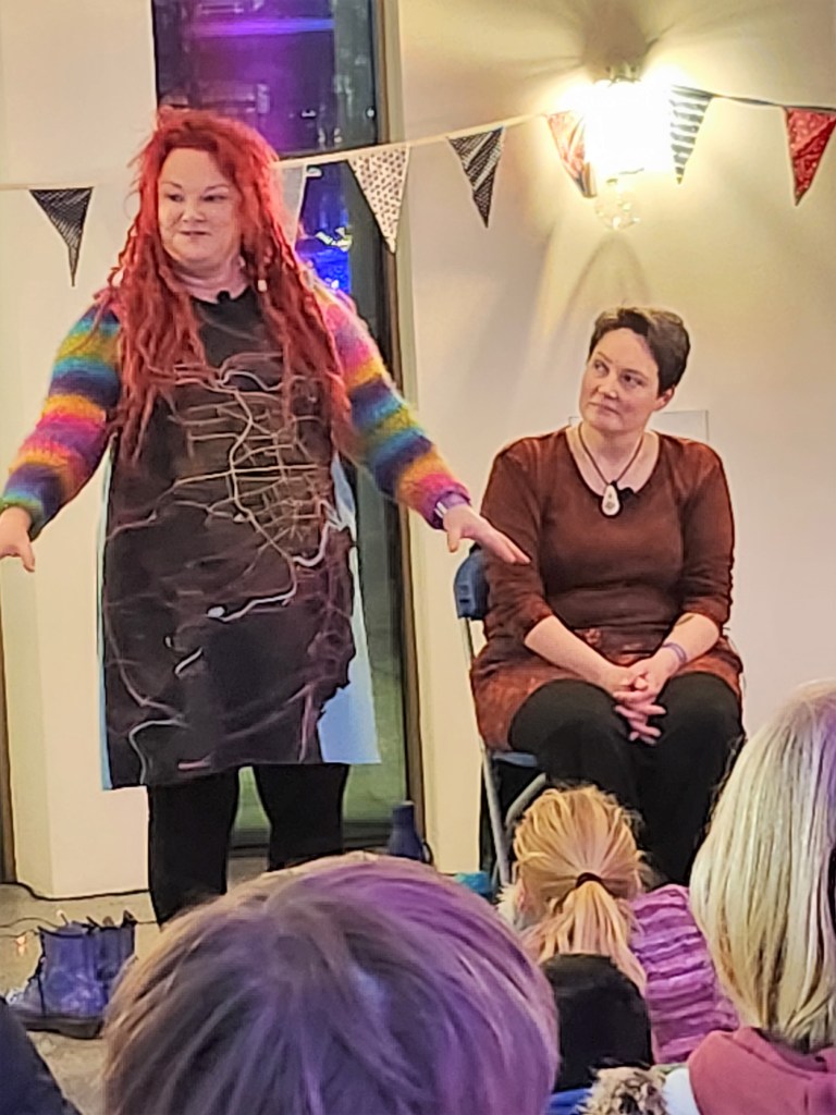 Pauline Cordiner and Lindsey Gibb tell stories at Spectra Light Festival 2023.
Pauline is standing talking to the crowd and Lindsey looks on. 